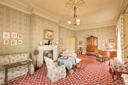 A photograph of the interior of Elizabeth Gaskell's house drawing room. It is furnished in period furniture with chintz fabrics and wallpaper.